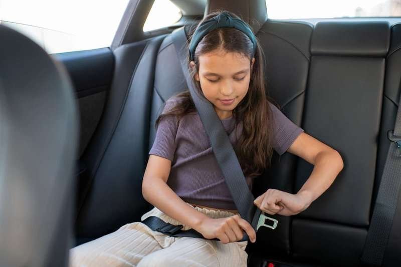 A girl fastens her seat belt in the back seat of a car