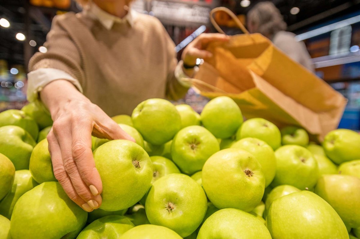 An elderly woman's hand holding a paper bag takes a fresh apple