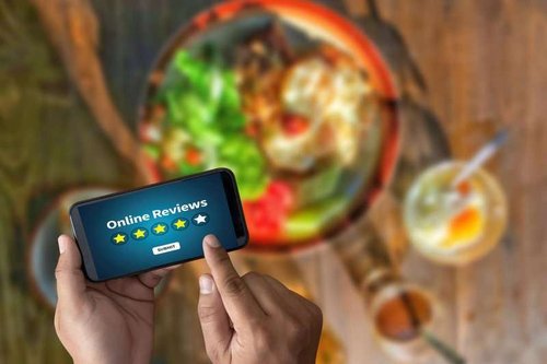 Close-up of a man holding a mobile phone and leaving a review of a restaurant