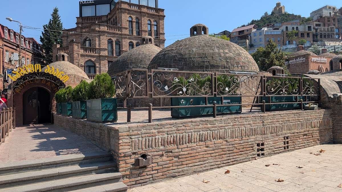 Brick domed rooftops of Tbilisi's historic sulfur bathhouses, with the "Royal Bath" entrance arch and Narikala Fortress on the hillside behind.