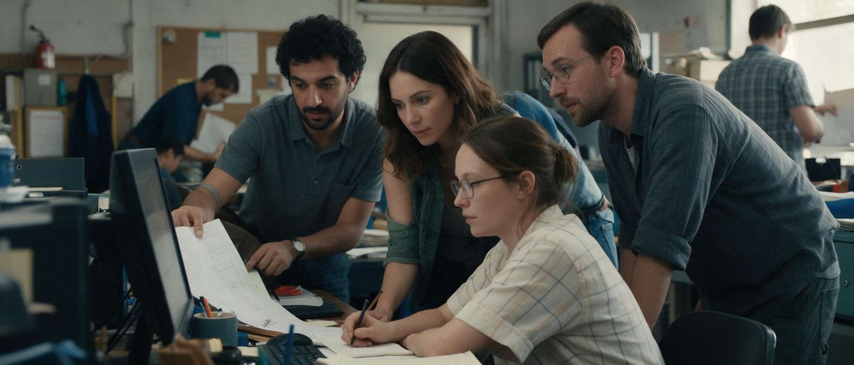 A team of engineers reviews technical drawings together at a busy design office, reflecting the local job market foreign workers weigh against Georgian salary levels.