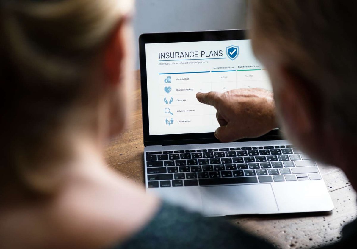 A person points to a laptop screen comparing insurance plans by monthly cost and coverage details, illustrating how to choose between policy options.