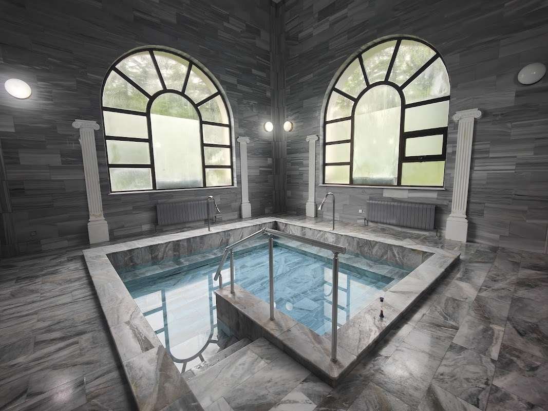 An empty marble-lined thermal pool with arched windows and columns inside a historic bathhouse in Tskhaltubo.