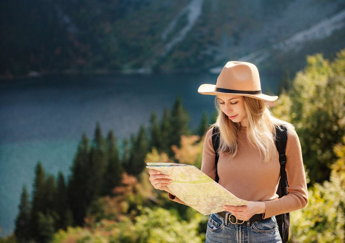 A hiker in a wide-brim hat studies a paper map beside a mountain lake, ready to plan her route through Georgia.