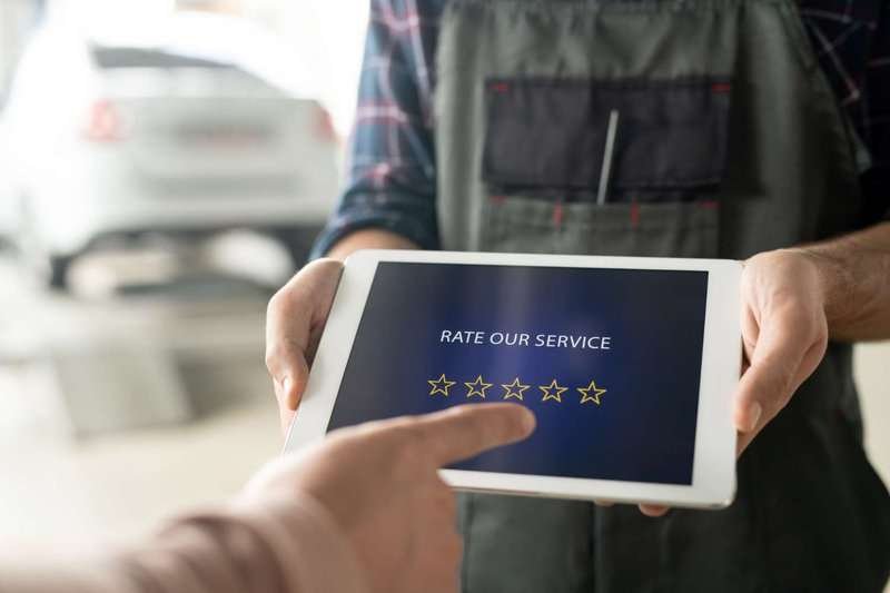 Hands of an auto service worker holding a touchpad with five stars on the screen while a customer is about to rate the service