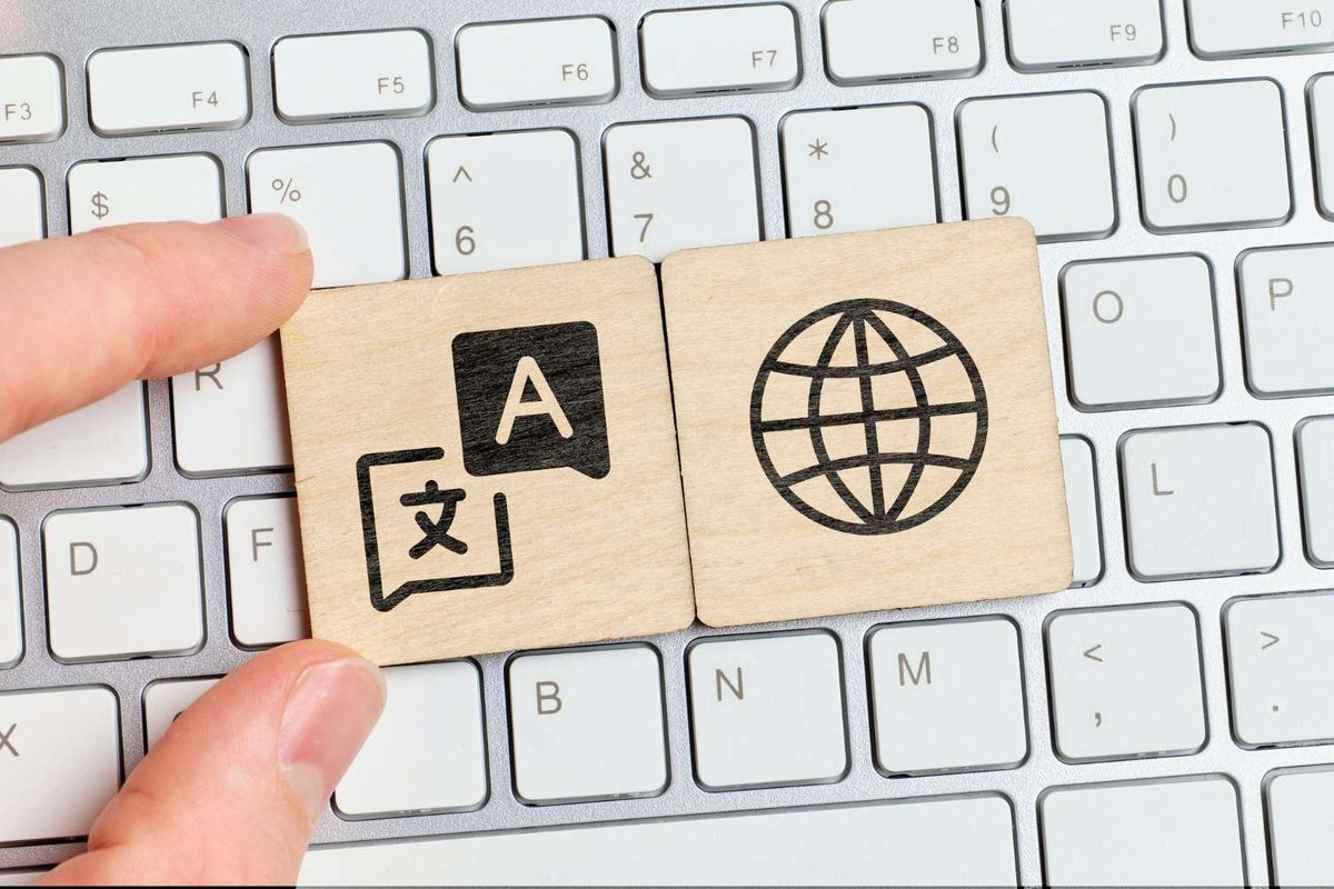 Wooden tiles with translation and globe icons held over a laptop keyboard, symbolizing document translation.