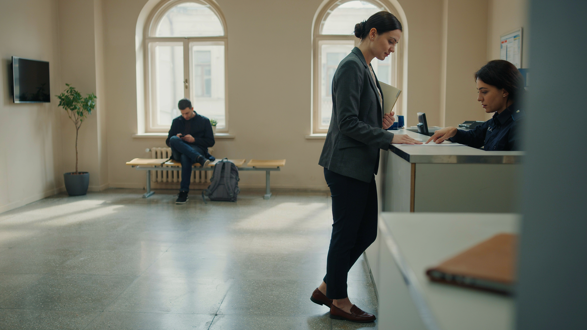 A professional woman submits documents at a government service counter while another applicant waits nearby, part of Georgia's new work permit (PTD) requirements for foreigners.