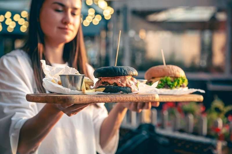 A girl holds a tray with several different burgers
