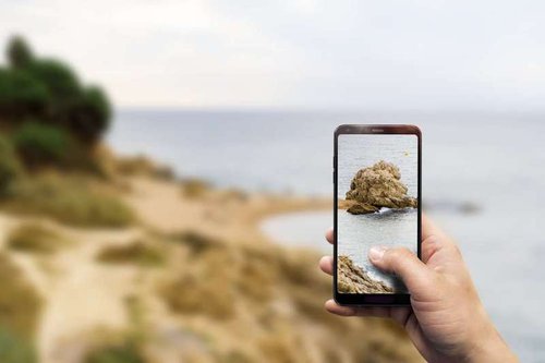 A man takes a photo of nature on a smartphone.