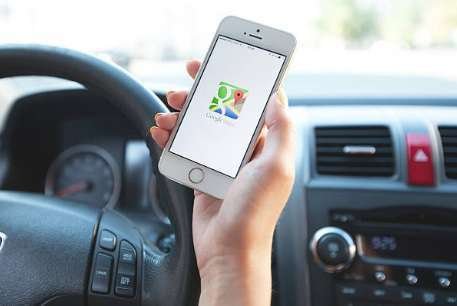 A man in a car holds a smartphone with the Google Maps app open