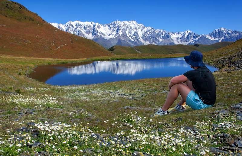 A young man sits near a lake and looks at the mountains in Svaneti.