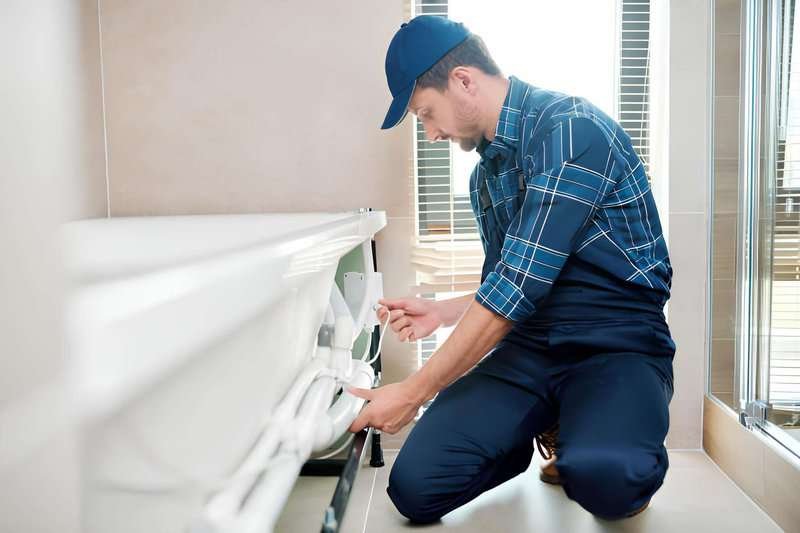 A plumber is replacing a drain trap under a bathtub.