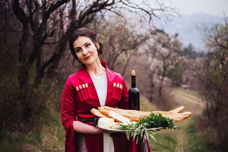 A girl in a Georgian costume with a large plate of lavash and a bottle of Georgian wine